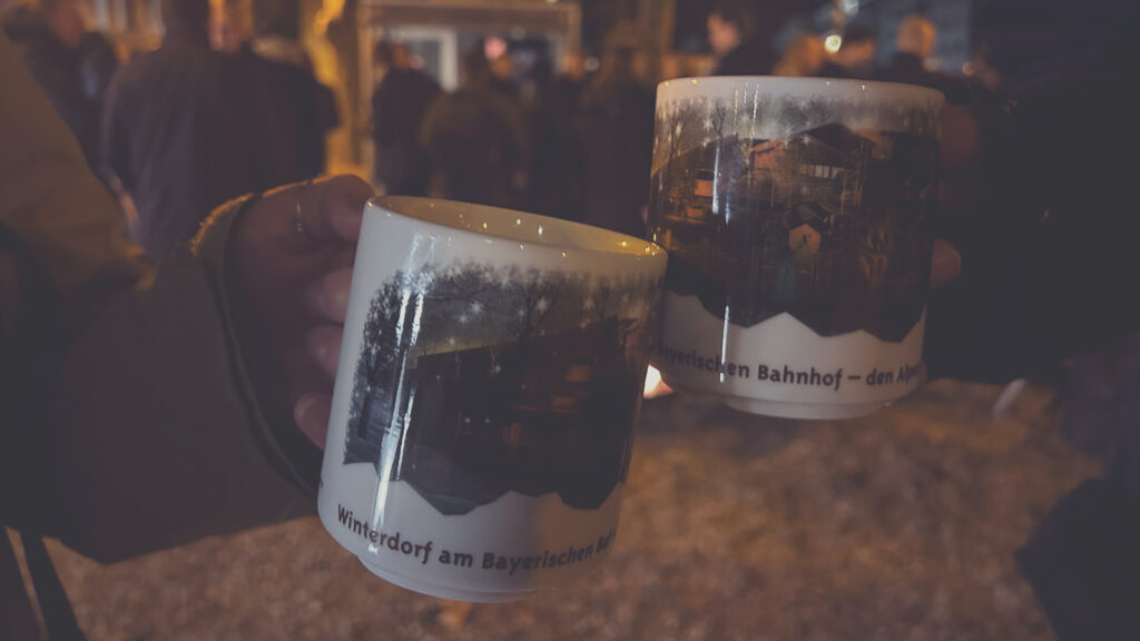 Zwei Personen stoßen mit Glühweintassen auf einem Weihnachtsmarkt an.